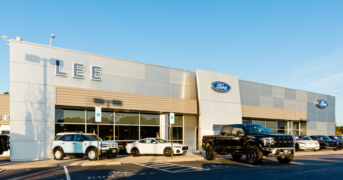 Exterior of Lee Ford dealership with a light blue Bronco, white Mustang, and black F-150 in the foreground.